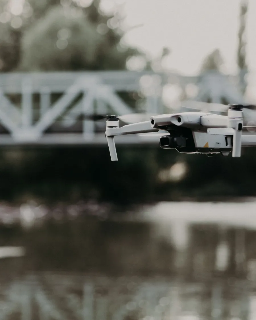 A quadcopter drone in flight near a steel bridge, used in ZoneOfWar hardware-in-the-loop labs